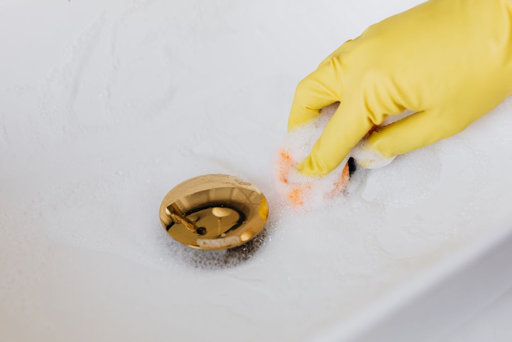 Main gantée de jaune au-dessus de la bonde d'un lavabo
